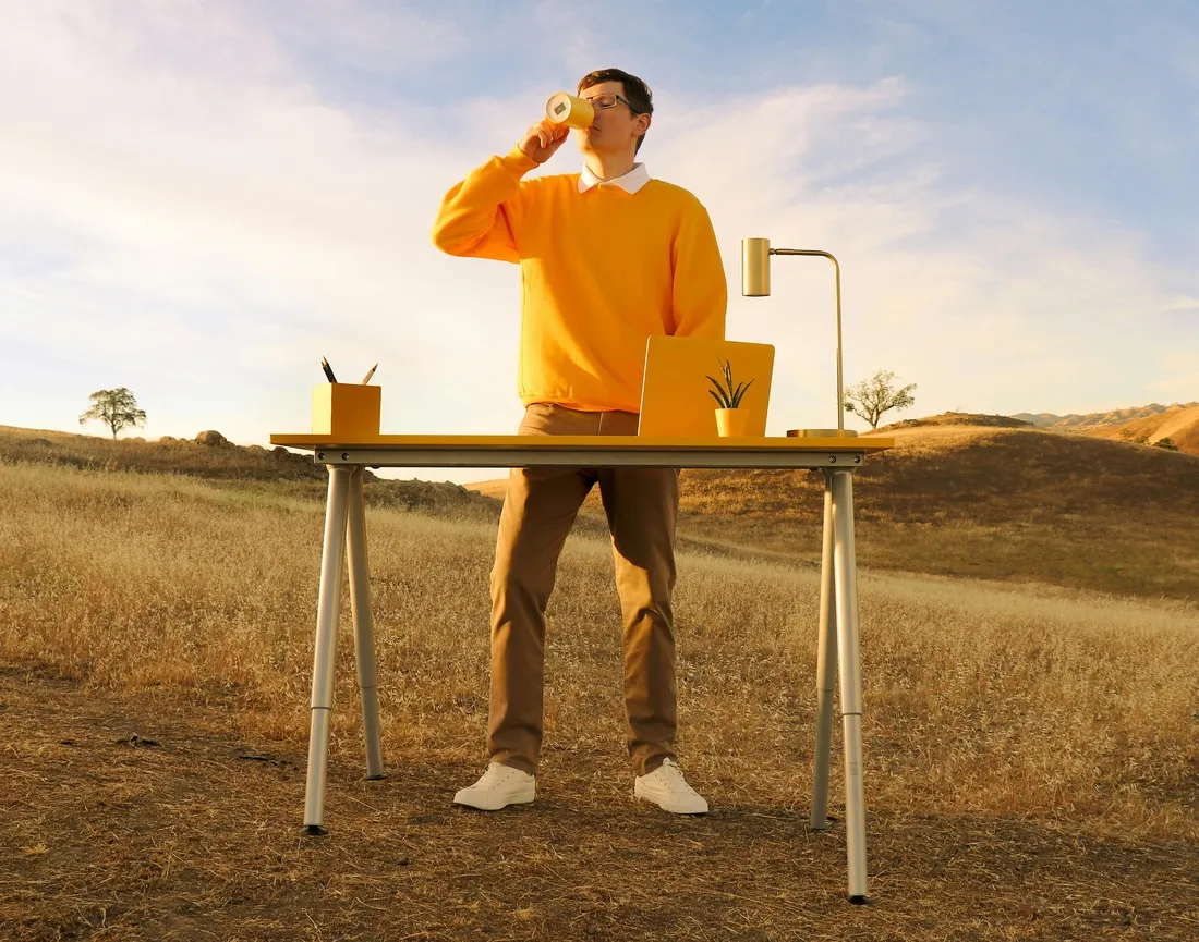 Homme debout en plein air buvant un café devant un bureau minimaliste, au lever du soleil