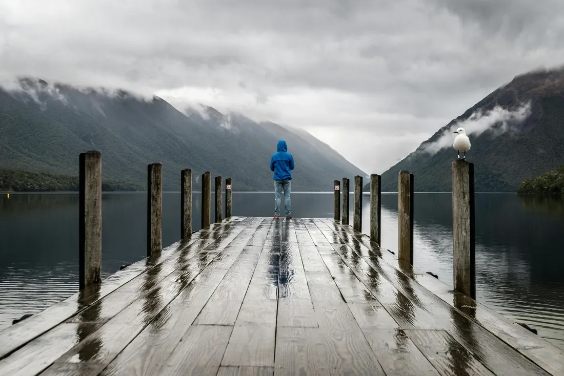 femme sur un pont au bord d'un lac avec des montagnes à l'horizon