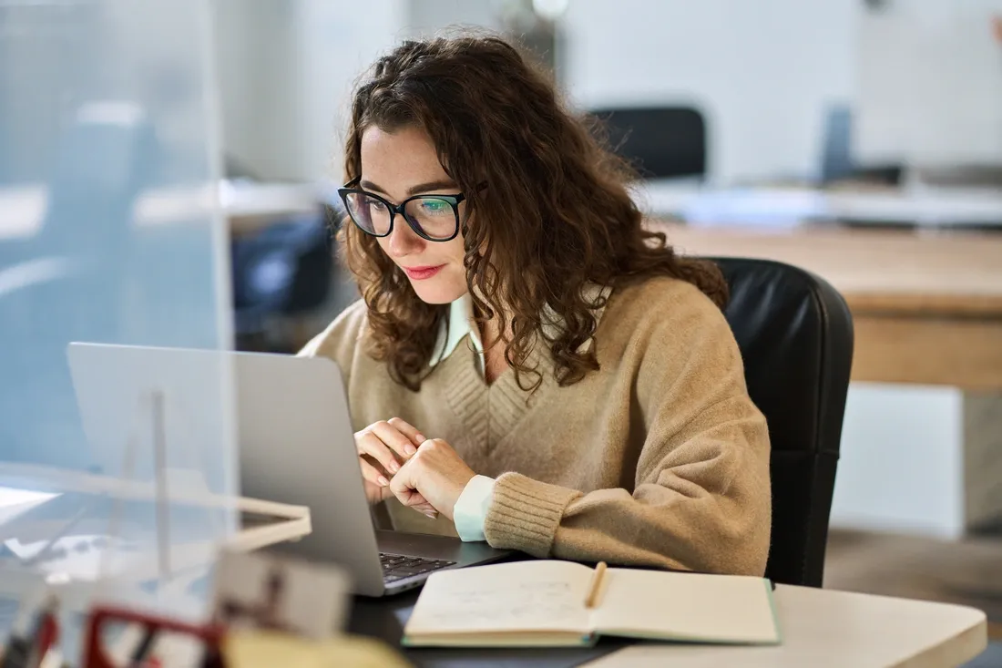 Femme travaillant sur un ordinateur portable dans un bureau avec un cahier à côté d'elle