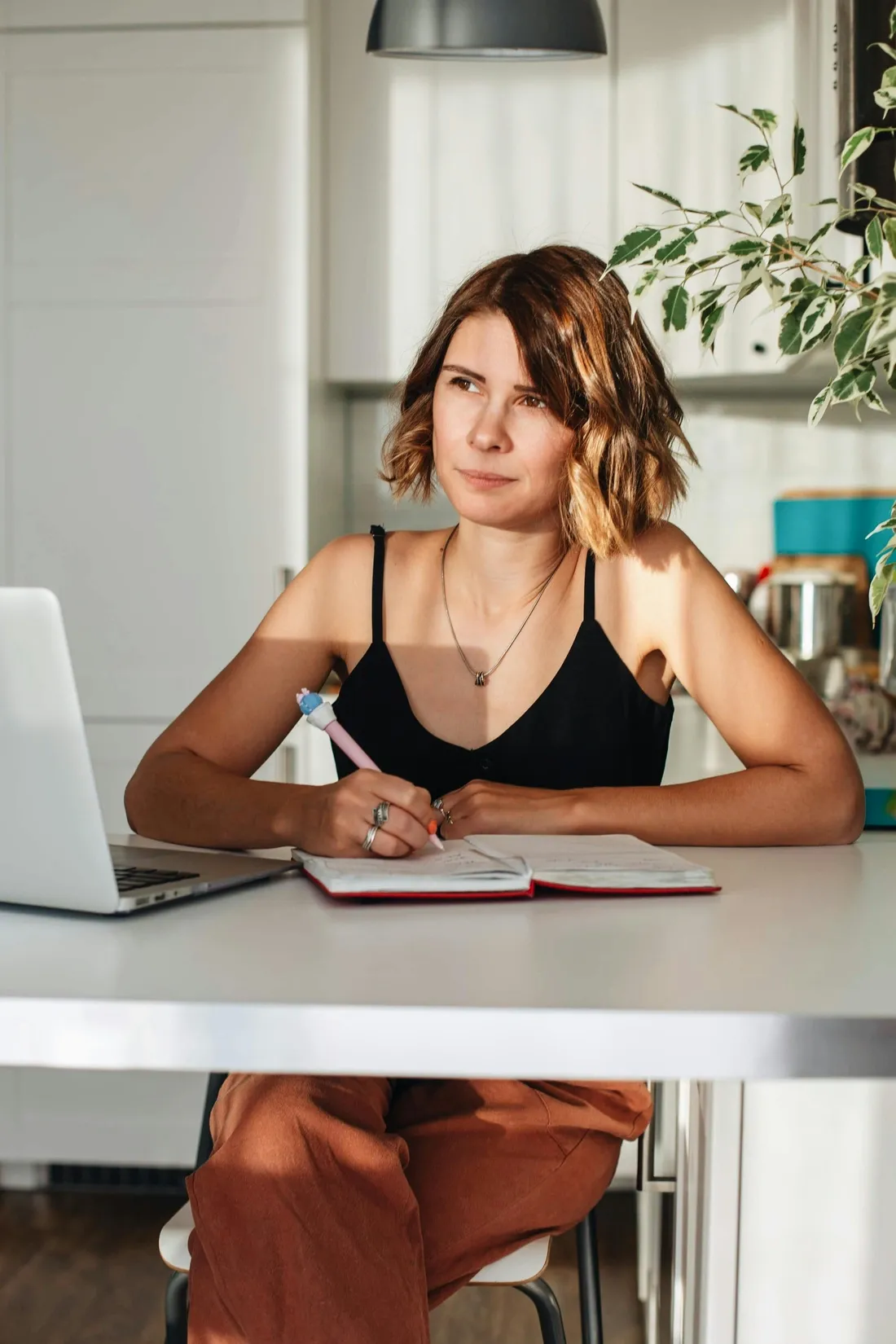Femme soleil dans les yeux assise avec son ordinateur portable ouvert et un stylo dans la main