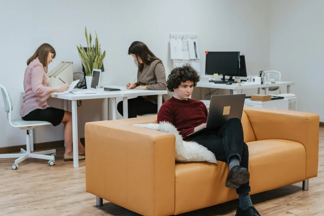 Un homme dans un open space assis sur un canapé utilisant son ordinateur portable